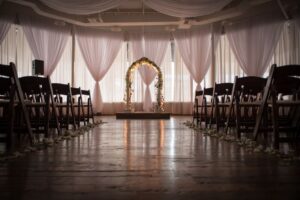 Beautiful wedding arch, lit up, large event hall, wood floor and chairs, dimly lit Beautiful wedding arch, lit up, large event hall, wood floor and chairs, dimly lit