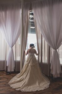 Pretty bride looking out of a full-length window draped in white Pretty bride looking out of a full-length window draped in white