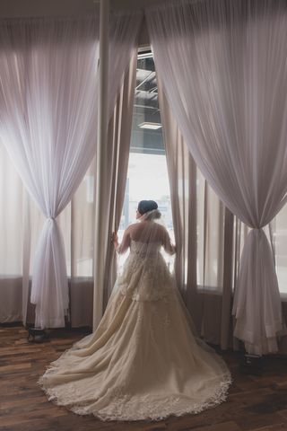 Pretty bride looking out of a full-length window draped in white