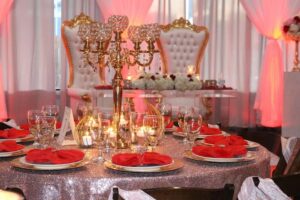 Round wedding table with gold, red and crystal decorations and dinnerware with 2 throne-like chairs in the background, 660 LaFayette Street Horton Events Downtown Nashville Round wedding table with gold, red and crystal decorations and dinnerware with 2 throne-like chairs in the background, 660 LaFayette Street Horton Events Downtown Nashville