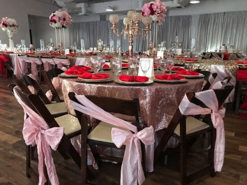 Round tables decorated with pink and gold glittery table cloth, white plates and red napkins, chairs with pink sashes, 660 LaFayette Street, Horton Events Downtown Nashville