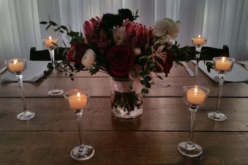 Longstem candle holders with small votives on a wood table with a floral arrangement in a glass vase, 660 LaFayette Street, Horton Events Downtown Nashville