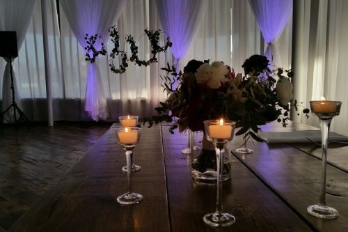 Beautiful long stem candle holders with votives, floral placeholder on a wooden table.