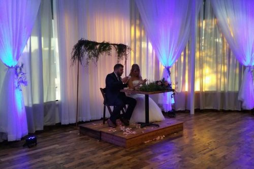 Bride and Groom on a platform opening cards in front of draped full length windows, 660 LaFayette Street, Horton Events Downtown Nashville