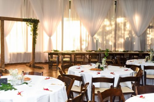 Round tables with white table cloths and wedding place settings with a wedding arch in front of full length windows with white drapes. Horton Events Downtown Nashville.