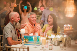 People at a birthday party cheering on the man with the birthday to blow out the candles