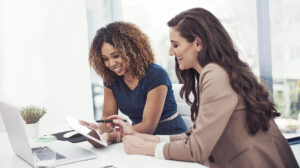 Two women in an office looking at a tablet and smiling