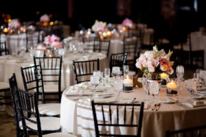 White linen tables set for an evening dinner with candles & floral bouquets.